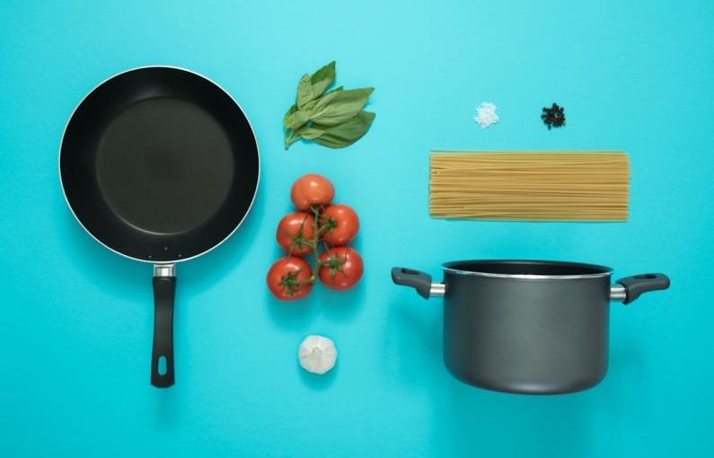 Kitchen Utensils - flat lay photography of frying pan beside tomatoes on blue surface